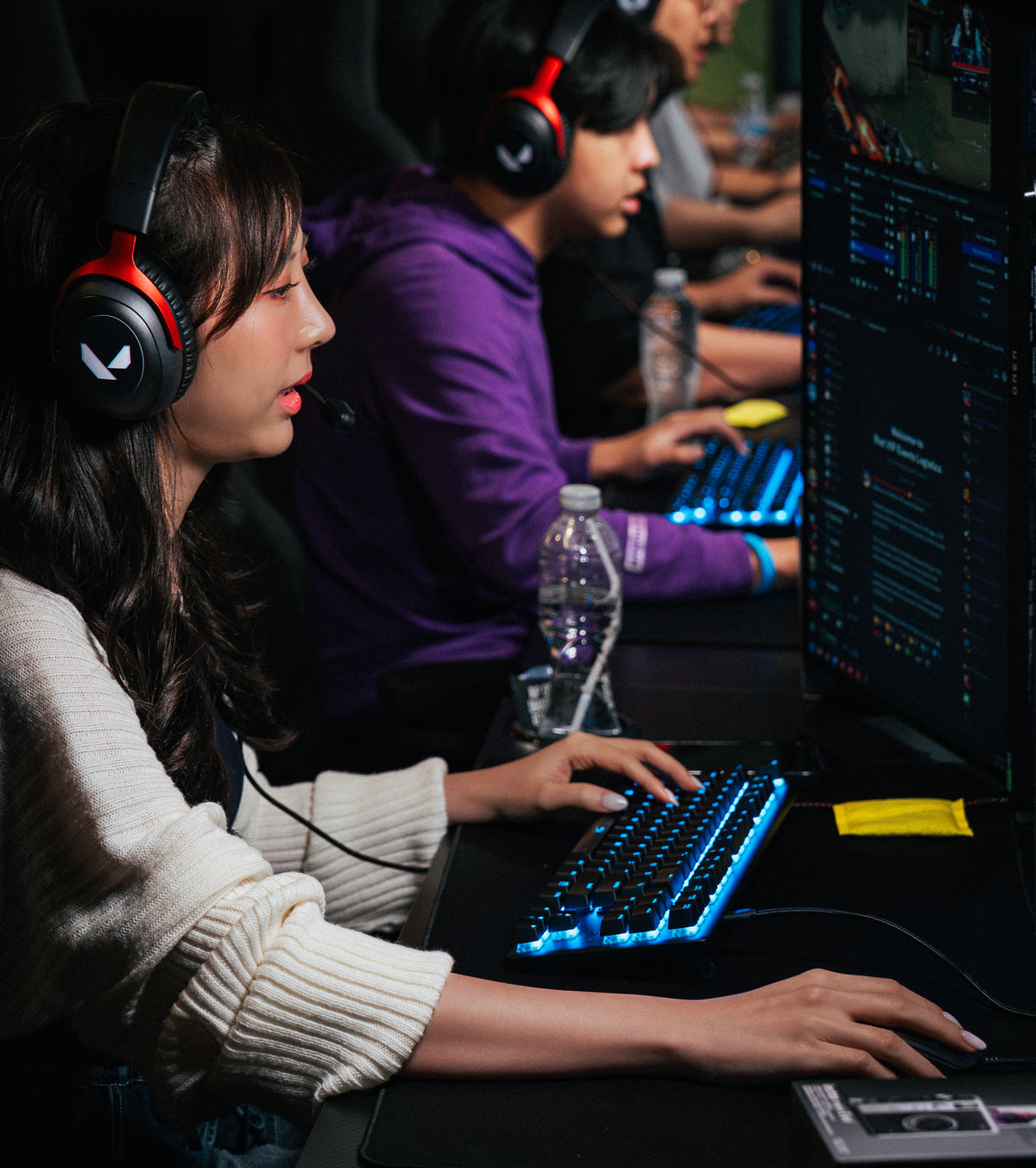 Players at gaming desks with a yellow PREFIRE pouch by the keyboard