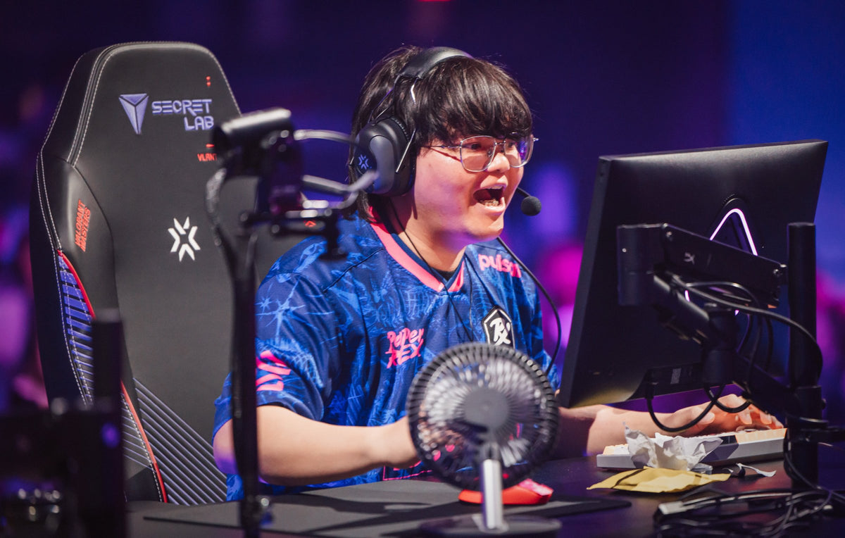 Paper Rex player laughing on stage with yellow pouches on the desk