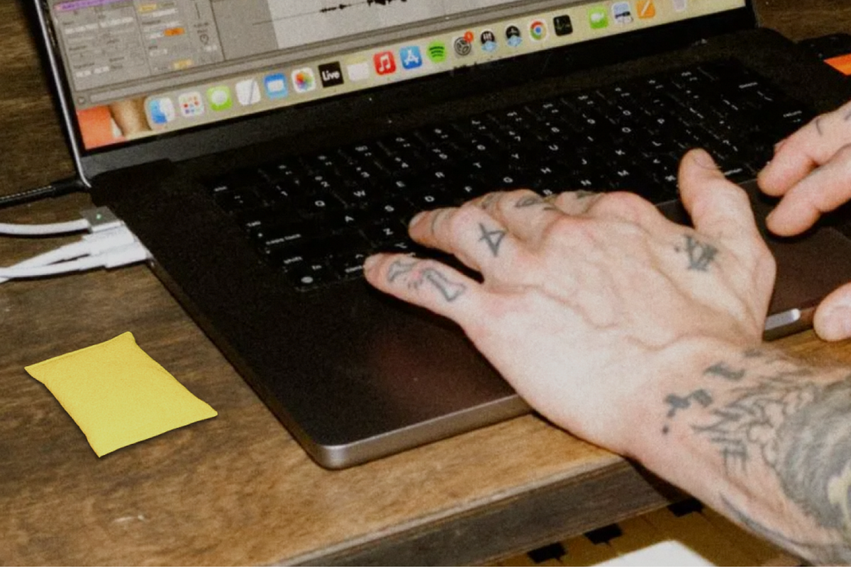 Tattooed hands typing on a laptop next to a yellow PREF*RE pouch