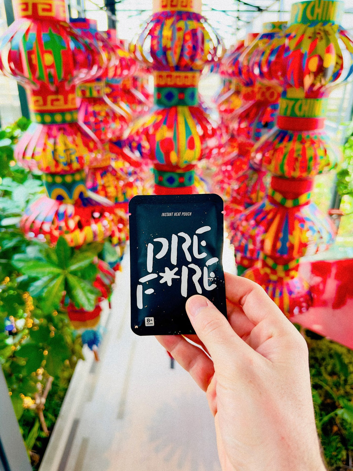 A black PREF*RE pouch held up in front of paper lanterns in Bangkok