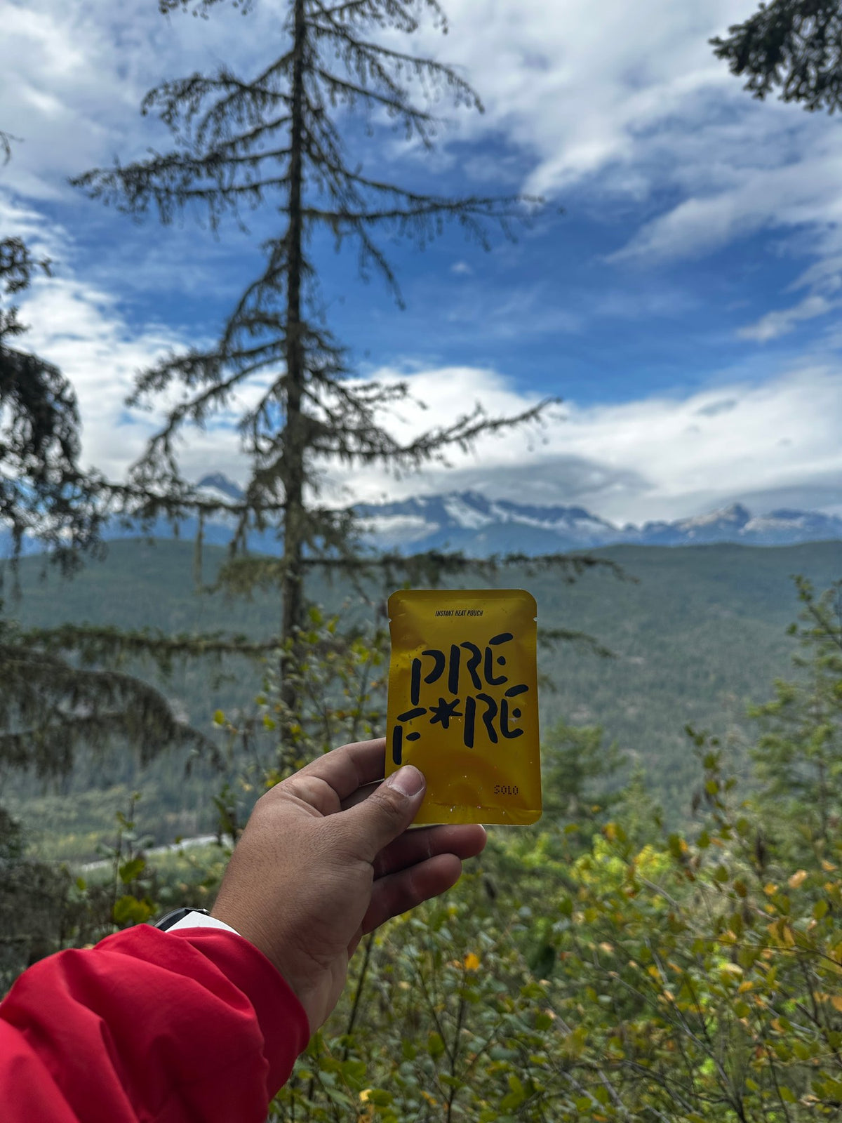 Hand holding a yellow PREFIRE pouch over a mountain view