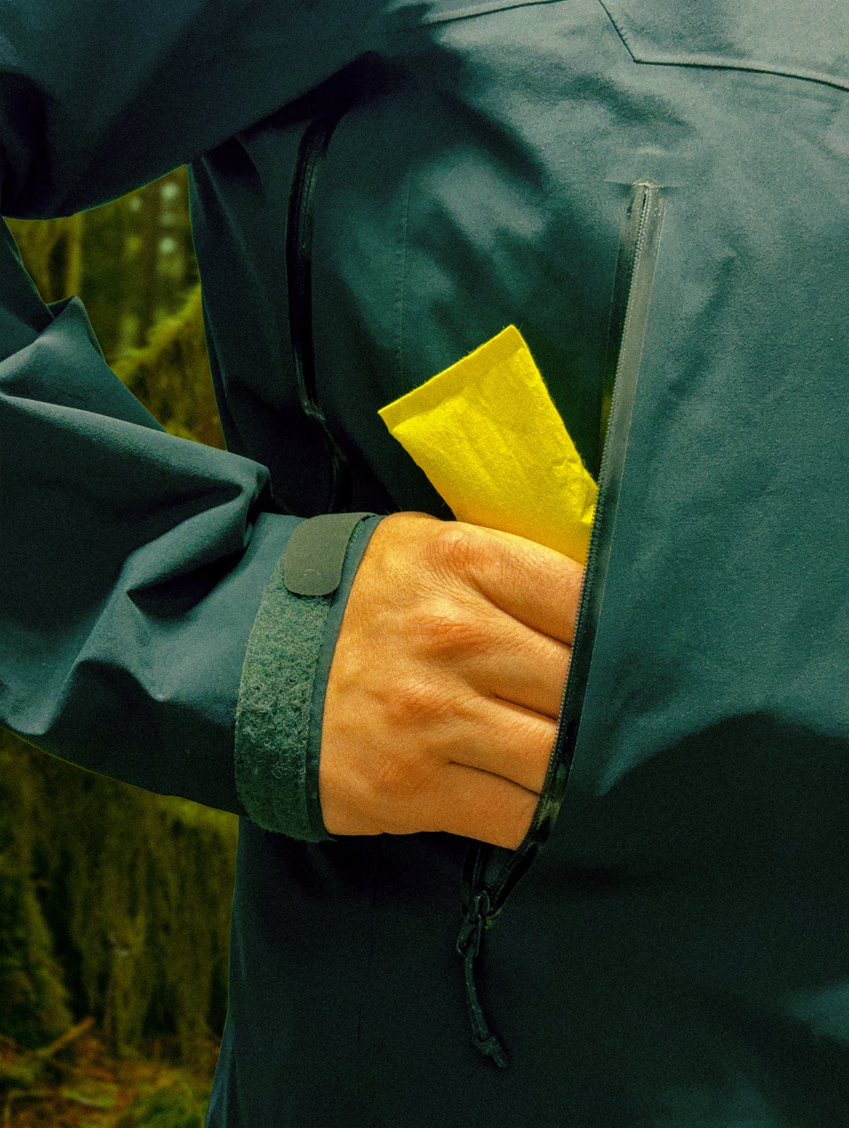 Hand in a jacket pocket with a yellow PREFIRE pouch in the forest